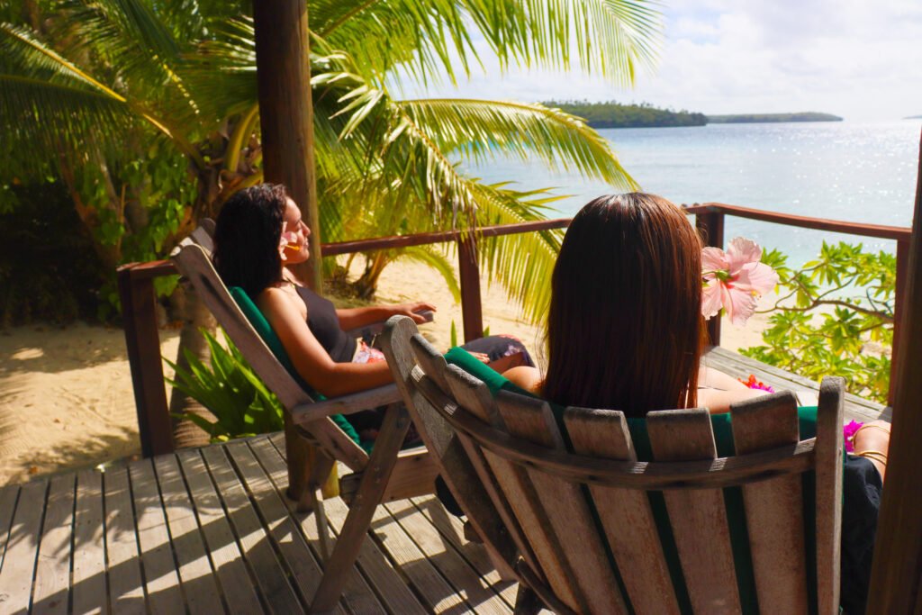 Two women sitting on wooden chairs on a balcony looking at the ocean