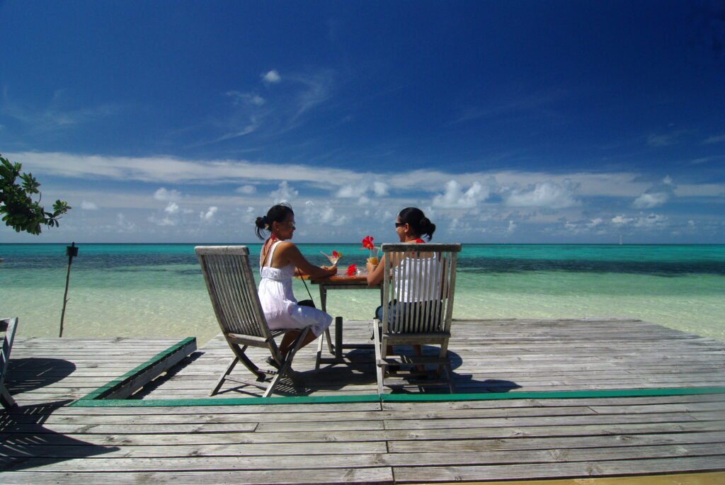 Two girls sitting on wooden chairs on a wooden deck facing the ocean