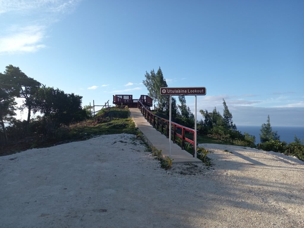 A hilltop sign with a wooden path winding down to the ocean, offering a beautiful view of the coastline